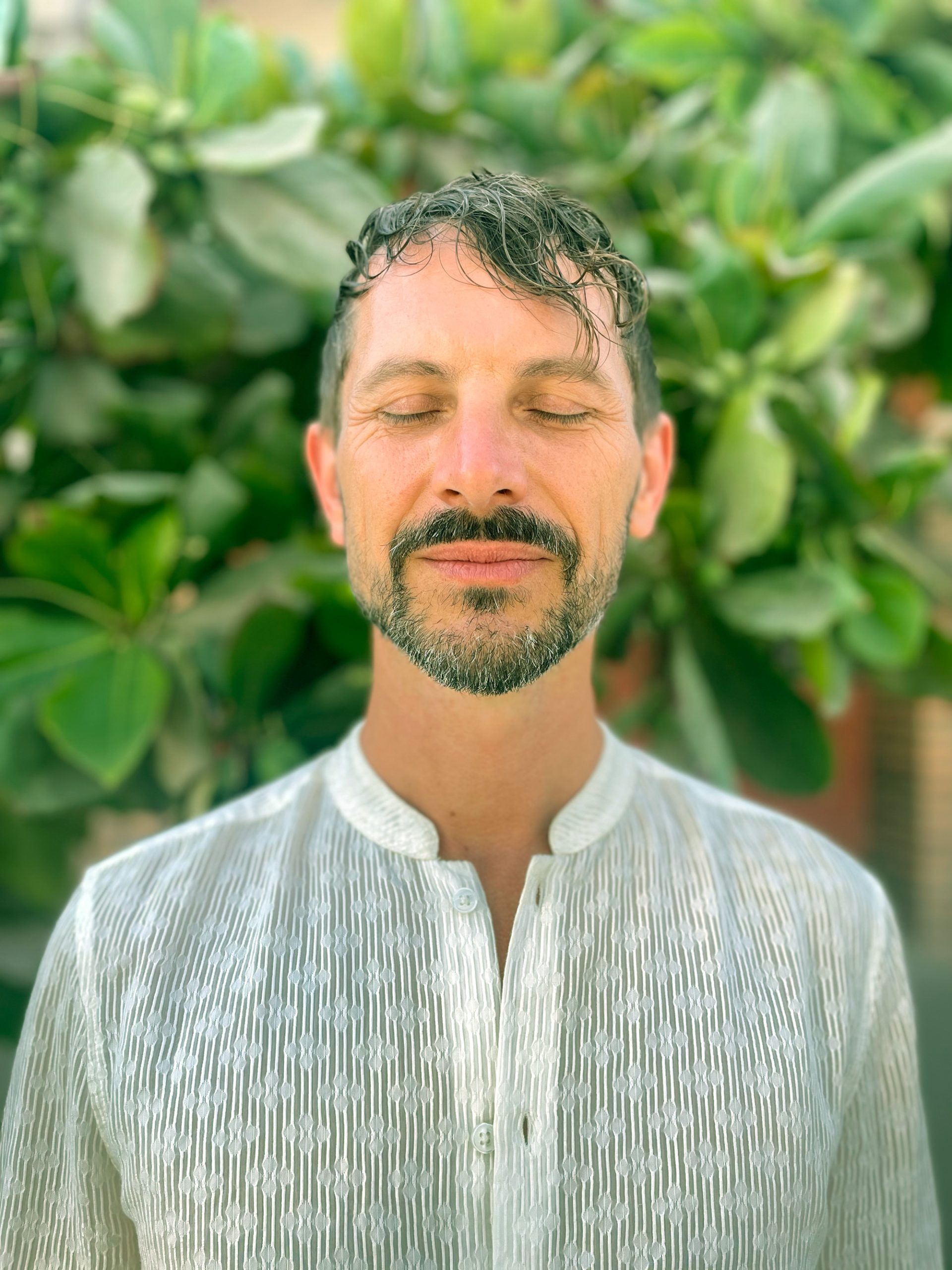 radiant-peace Smiling man with eyes closed in front of lush green leaves, embodying inner peace and grounded strength.